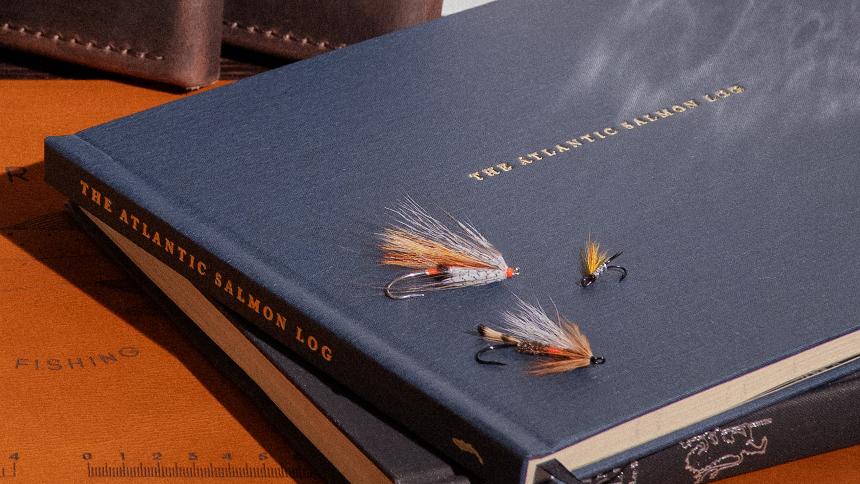 Front cover of the Atlantic Salmon Log, a handcrafted fishing journal for salmon anglers with Atlantic salmon flies on top.