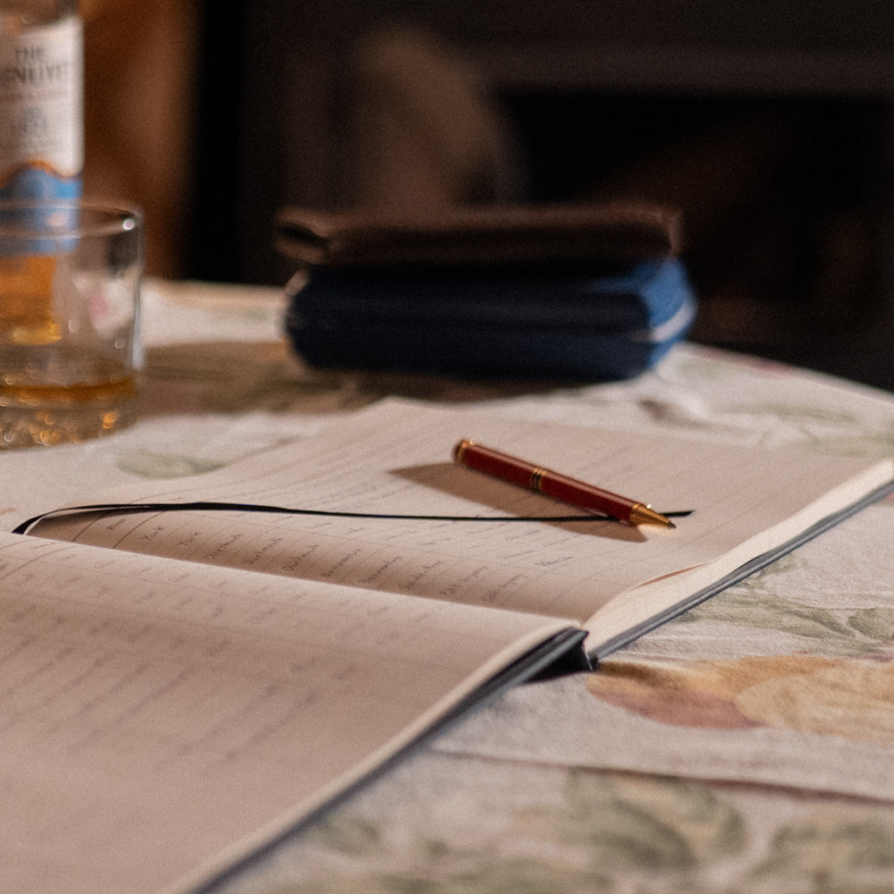 Interior pages of the Atlantic Salmon Log showing fields to record fly, river, and conditions with a red pen, and a bottle of Scotch.