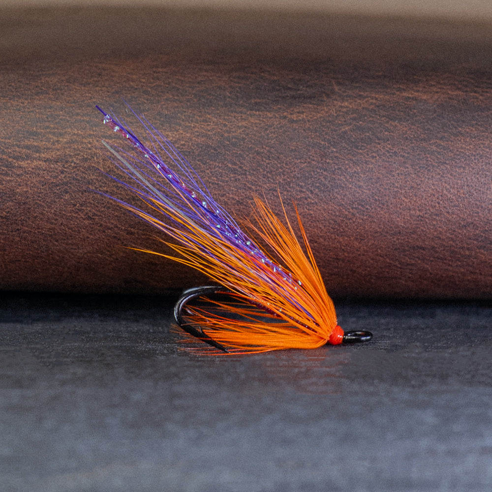 Orange and purple double hook Atlantic salmon fly, the Grant's Orange, on a brown leather surface