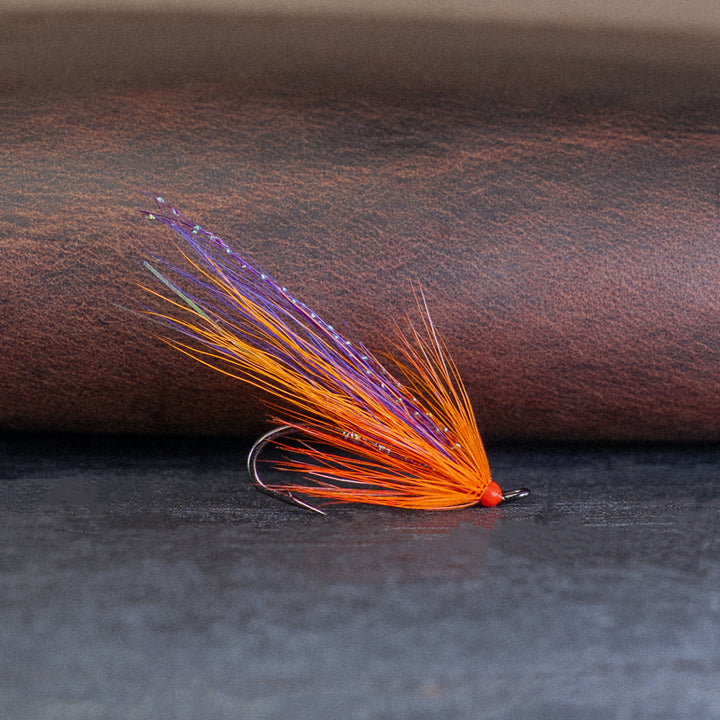 Orange and purple single hook Atlantic salmon fly, the Grant's Orange, on a brown leather surface