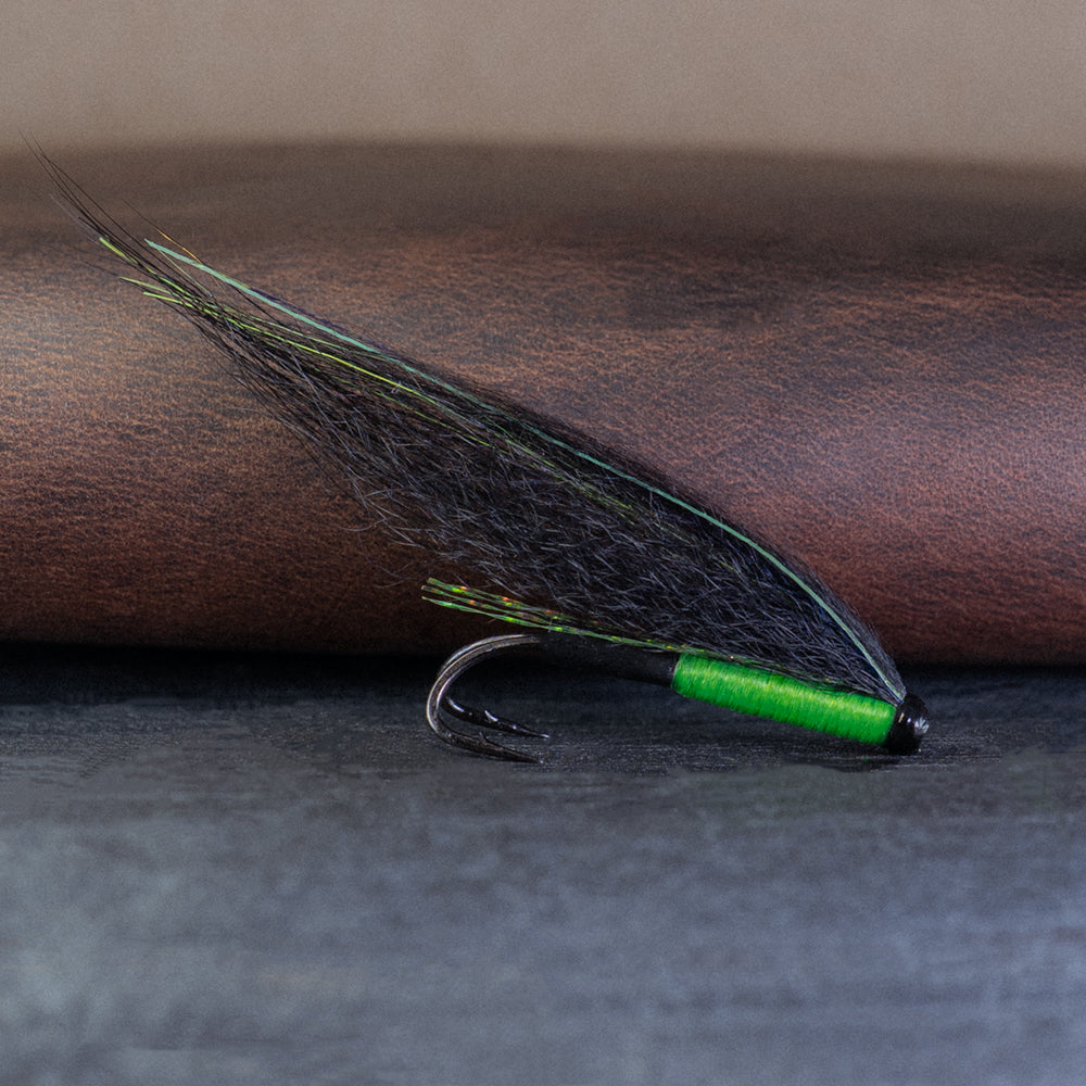 Atlantic salmon tube fly with green body and black wing, called the ViMu, with a leather fly wallet in the background.