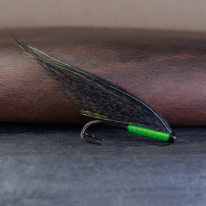Atlantic salmon tube fly with green body and black wing, called the ViMu, with a leather fly wallet in the background.