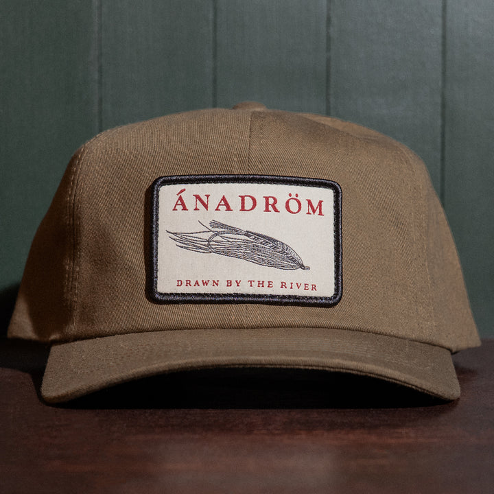 Olive cap with a salmon fly patch featuring the brand 'ÁNADRÖM' on a dark background