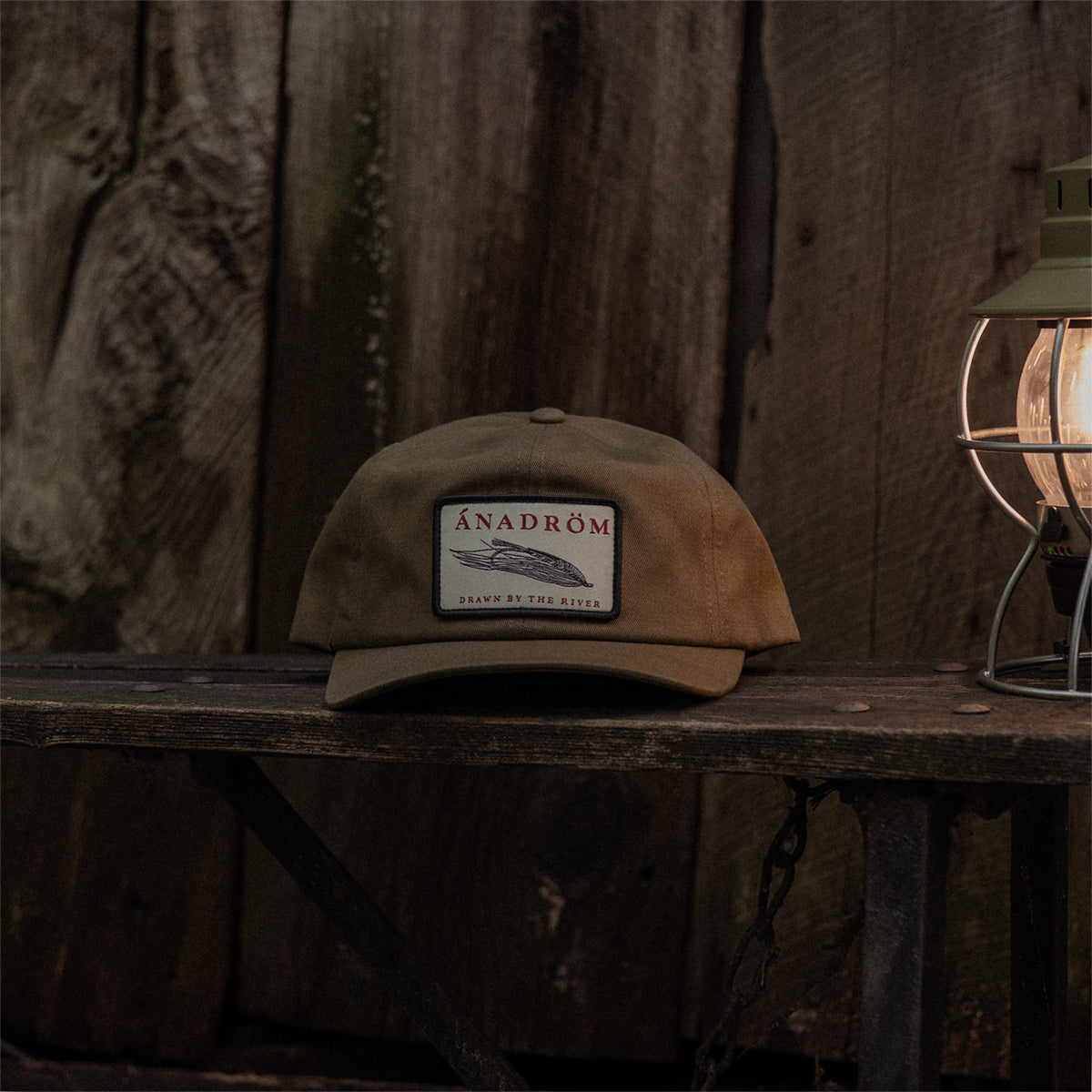 Olive cap with a salmon fly patch on a wooden surface with a rustic background