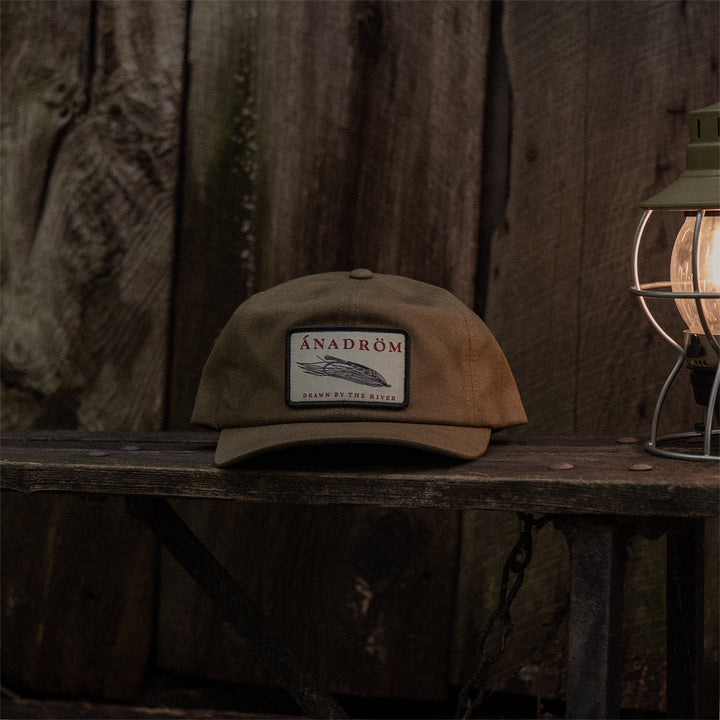 Olive cap with a salmon fly patch on a wooden surface with a rustic background