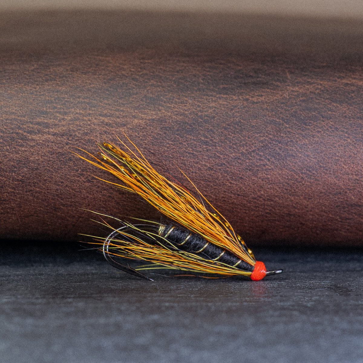 Atlantic salmon fly with yellow, orange and black hair, called the Willie Gunn, on a brown leather surface