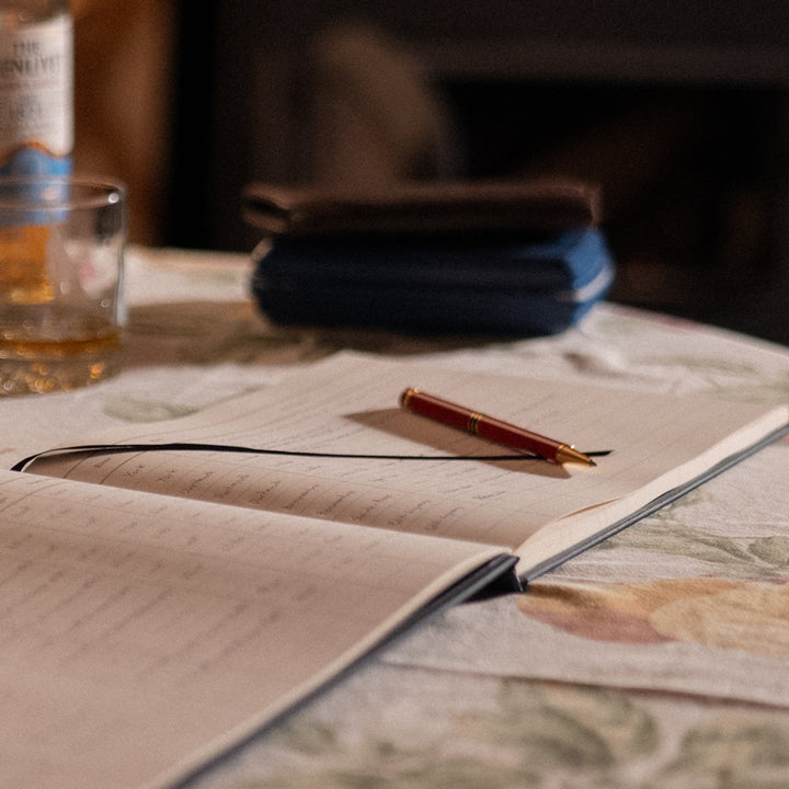 Interior pages of the Atlantic Salmon Log showing fields to record fly, river, and conditions with a red pen, and a bottle of Scotch.