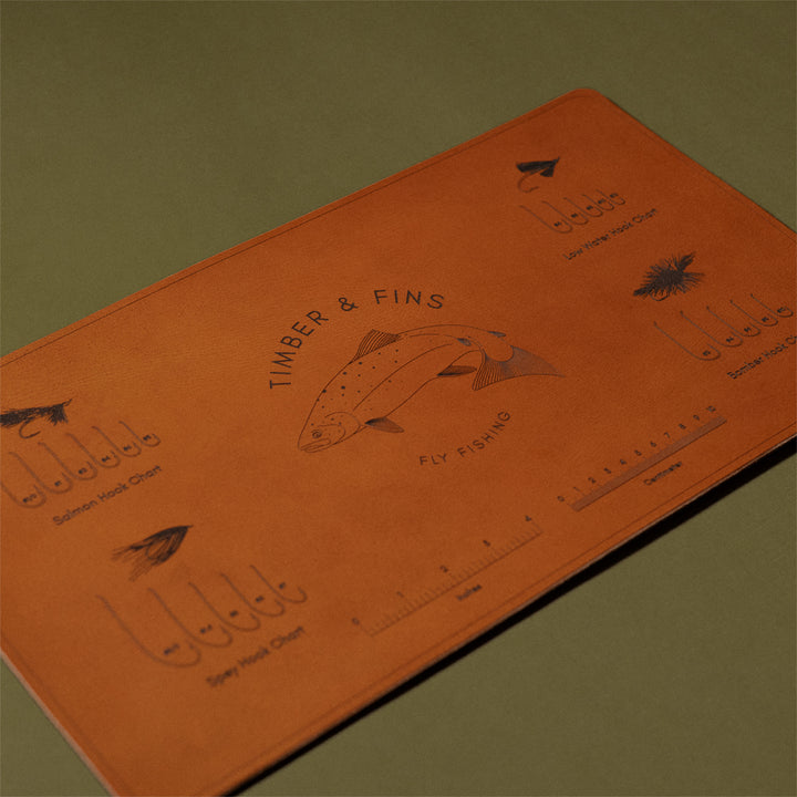 Fly tying mat photographed on a green background at an angle, showing salmon hook charts and ruler guides for tiers
