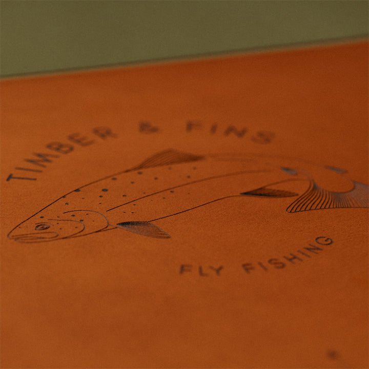 Detailed view of the Atlantic salmon logo at the center of the Timber & Fins fly tying mat, surrounded by size charts and ruler lines