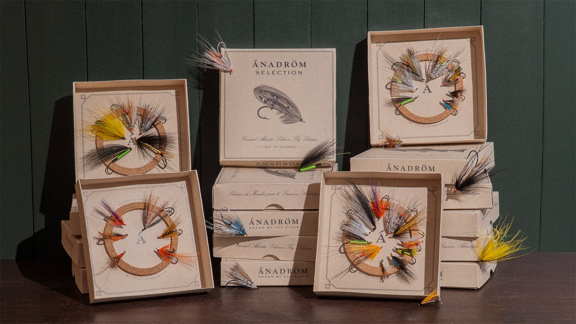 Wide shot of Ánadröm's full collection of fly assortment boxes, with four open fly boxes displaying Atlantic salmon fly selections, dark green backdrop.