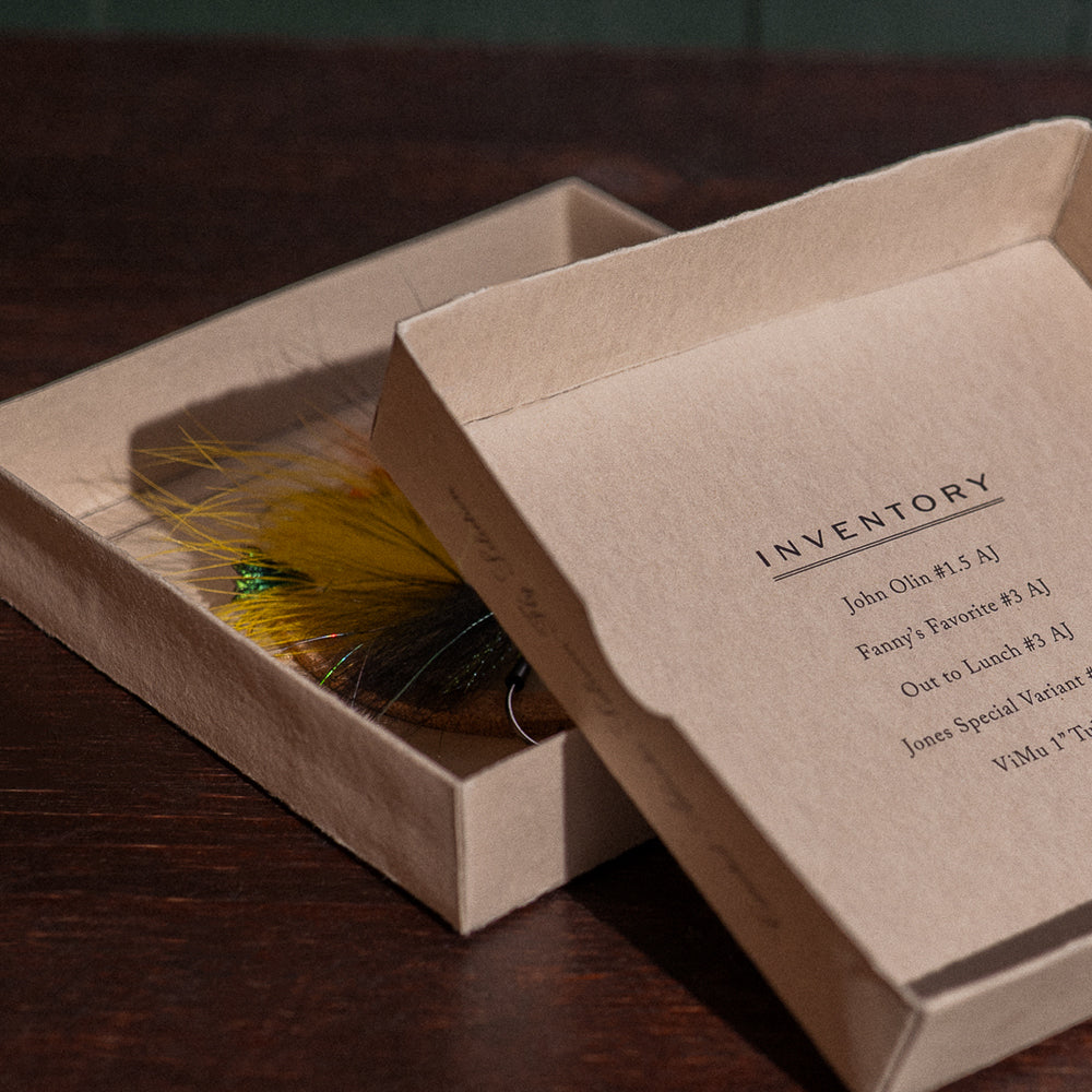 Ánadröm Early Season fly box open beside inventory lid, yellow and black Quebec-tied salmon flies visible.