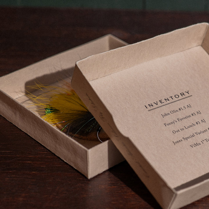 Ánadröm Early Season fly box open beside inventory lid, yellow and black Quebec-tied salmon flies visible.
