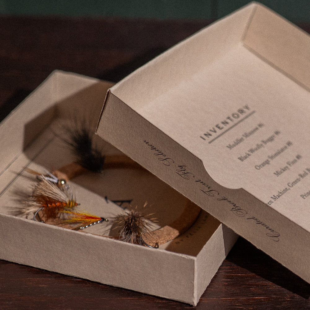 Ánadröm Brook Trout Selection fly box open beside inventory lid, dry flies and streamers on cork insert.